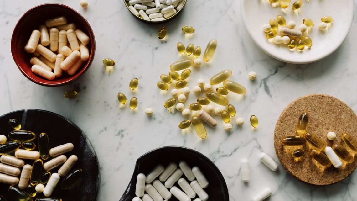 Variety of capsules and pills displayed in bowls on a marble table, ideal for healthcare concepts.
