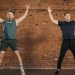 Two men performing jumping jacks in a gym setting, showcasing fitness and energy.